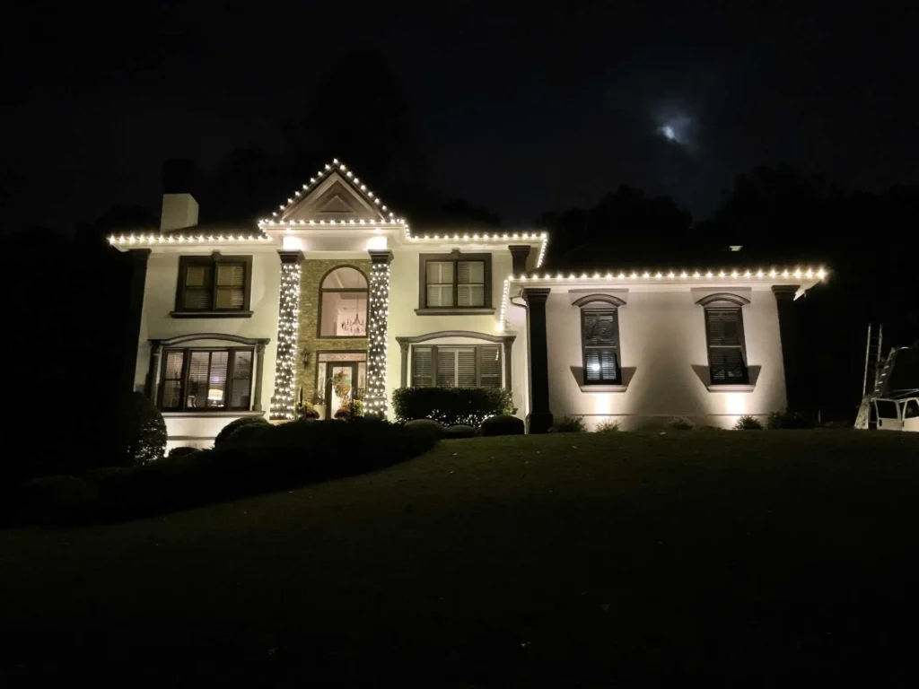 White roofline holiday lights illuminating a large Atlanta-area home at night.